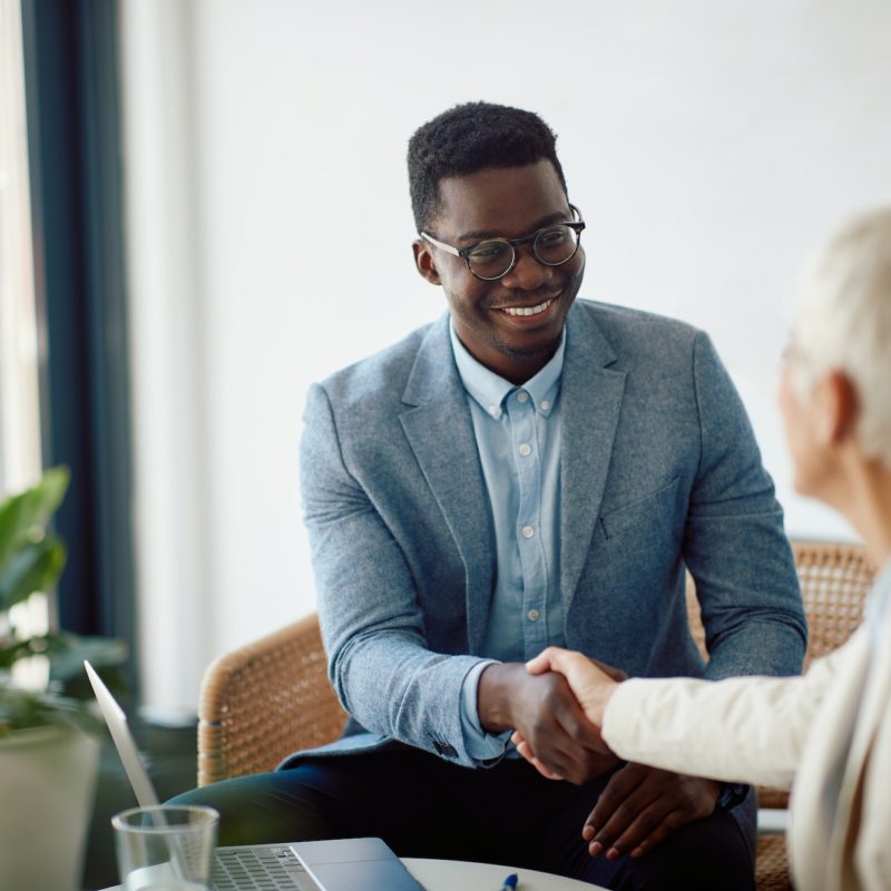 Happy black entrepreneur shaking hands with female colleague during business meeting in the office.