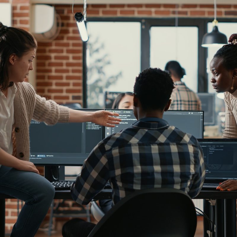 System engineer sitting on desk discussing with mixed team of coders about ai innovation